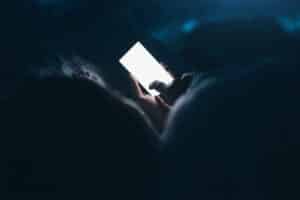 Woman texting and reading on smartphone in bed