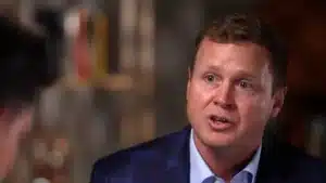 Man in a blue blazer speaks during a discussion, with a blurred background.