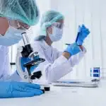 Scientist in PPE using a microscope in a bright laboratory environment.
