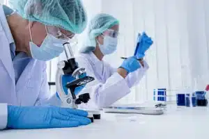 Scientist in PPE using a microscope in a bright laboratory environment.