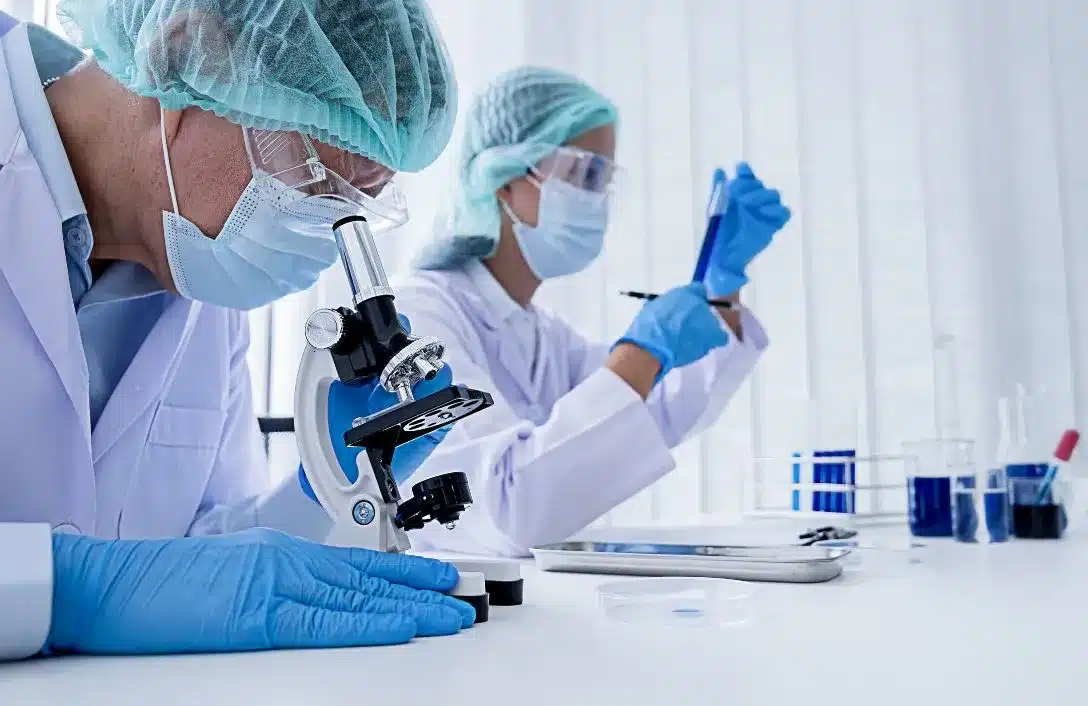 Scientist in PPE using a microscope in a bright laboratory environment.