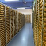 Corridor of metal racks filled with neatly stacked gold bars in a secure storage vault, viewed from one end.