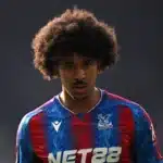 Young male footballer with big curly hair wearing a blue and red Crystal Palace jersey, looking intently ahead on the pitch.