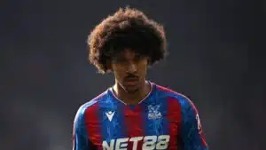 Young male footballer with big curly hair wearing a blue and red Crystal Palace jersey, looking intently ahead on the pitch.