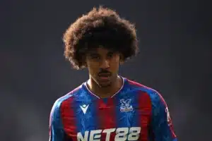 Young male footballer with big curly hair wearing a blue and red Crystal Palace jersey, looking intently ahead on the pitch.