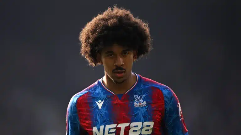 Young male footballer with big curly hair wearing a blue and red Crystal Palace jersey, looking intently ahead on the pitch.