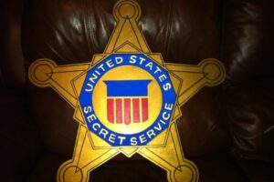 Gold star-shaped badge on brown leather background, with a blue circular seal reading United States Secret Service and a red striped shield at center.