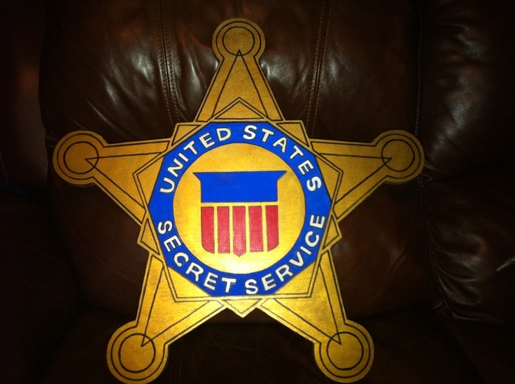 Gold star-shaped badge on brown leather background, with a blue circular seal reading United States Secret Service and a red striped shield at center.