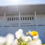 Front of the Donald J. Trump and John F. Kennedy Memorial Center for the Performing Arts, with blurred white and yellow flowers in the foreground.