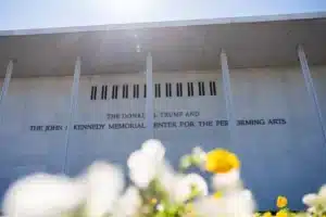 Front of the Donald J. Trump and John F. Kennedy Memorial Center for the Performing Arts, with blurred white and yellow flowers in the foreground.