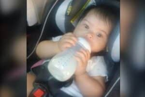 Baby seated in a car seat, drinking from a bottle.