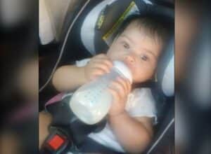 Baby seated in a car seat, drinking from a bottle.