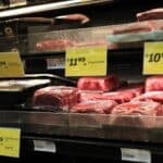 Beef meat in a grocery display case with yellow price tags showing prices like $10.99 and $11.49 on the minced/packed cuts