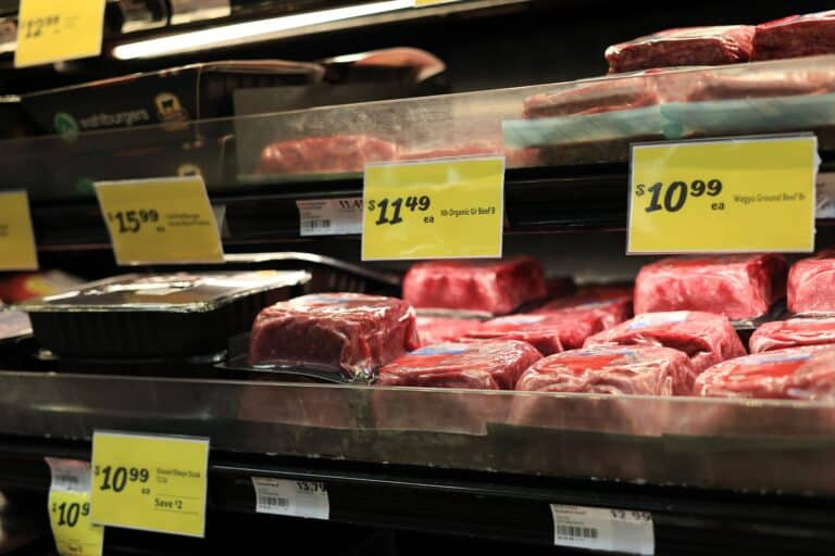 Beef meat in a grocery display case with yellow price tags showing prices like $10.99 and $11.49 on the minced/packed cuts