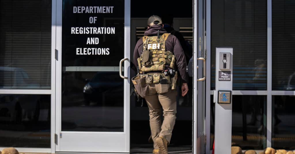 FBI agent in tactical vest enters a government office labeled Department of Registration and Elections.