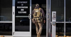FBI agent in tactical vest enters a government office labeled Department of Registration and Elections.