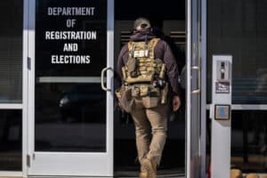 FBI agent in tactical vest enters a government office labeled Department of Registration and Elections.
