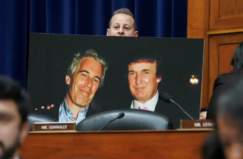 Poster of two smiling men in suits displayed on a desk in a formal hearing room, with a blurred foreground and a nameplate reading 'MR. CONNOLLY'
