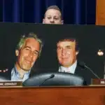Poster of two smiling men in suits displayed on a desk in a formal hearing room, with a blurred foreground and a nameplate reading 'MR. CONNOLLY'