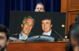 Poster of two smiling men in suits displayed on a desk in a formal hearing room, with a blurred foreground and a nameplate reading 'MR. CONNOLLY'