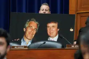 Poster of two smiling men in suits displayed on a desk in a formal hearing room, with a blurred foreground and a nameplate reading 'MR. CONNOLLY'