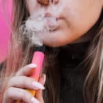 A,Young,Girl,Smokes,Disposable,Electronic,Cigarette.,Bright,Yellow,Background