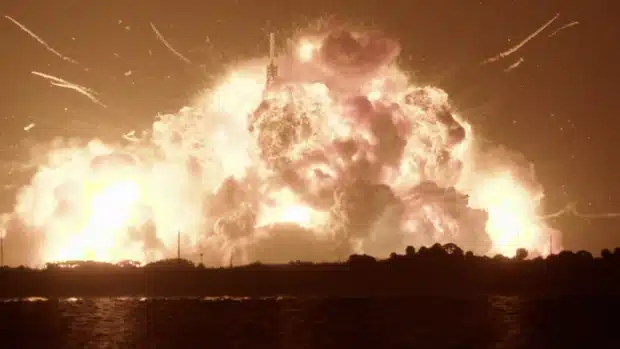 Nighttime rocket launch pad explosion with a massive orange fireball and thick smoke rising over the facility.