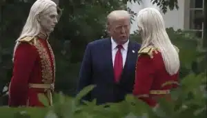 Donald Trump standing between two guards in red ceremonial uniforms with gold trim outdoors.