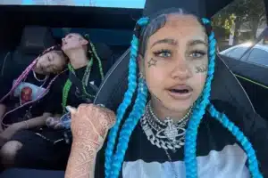 Front-seat person with bright blue braids, face tattoos, nose ring and heavy jewelry in a car; two friends sleeping in the back seat with pink and green braids.