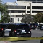 Police cars line a street in front of a Chase building, with yellow caution tape across the foreground indicating a restricted area.