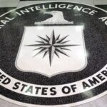 Circular CIA seal on the floor with the words 'Central Intelligence Agency' surrounding a white shield bearing a black compass rose and an eagle above it