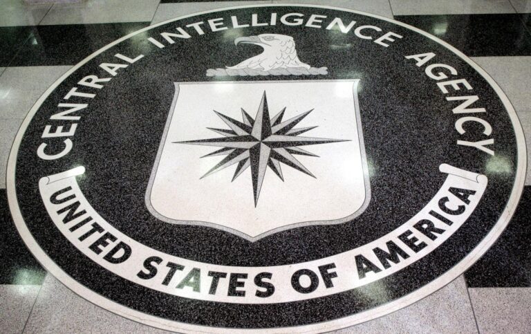 Circular CIA seal on the floor with the words 'Central Intelligence Agency' surrounding a white shield bearing a black compass rose and an eagle above it