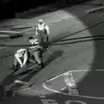 Two workers in safety vests pull on a rope on a dimly lit street at night.