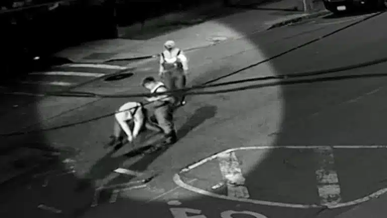 Two workers in safety vests pull on a rope on a dimly lit street at night.