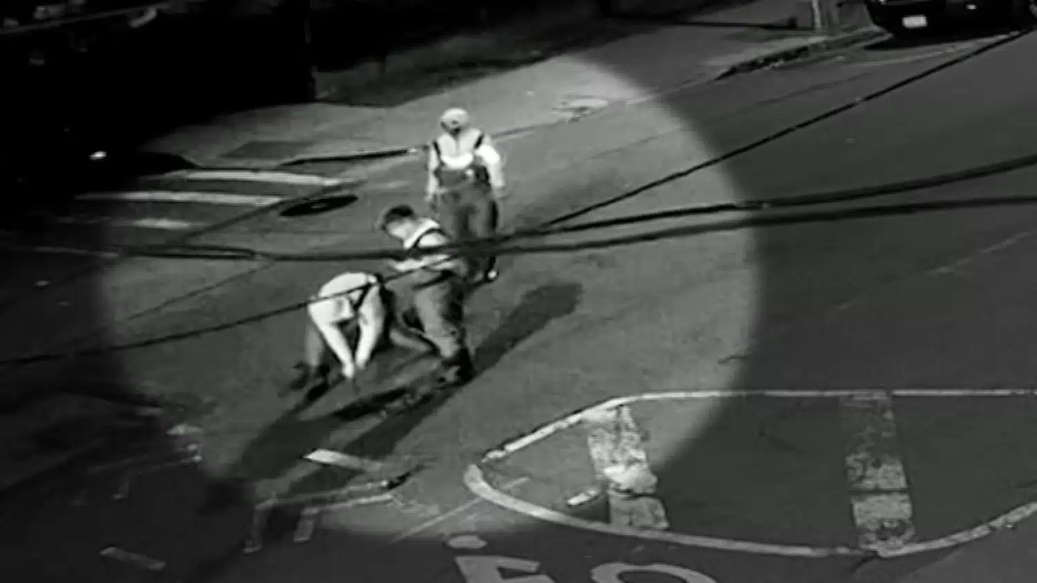 Two workers in safety vests pull on a rope on a dimly lit street at night.
