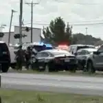 Emergency scene on a highway with police cars and flashing lights amid several parked vehicles, three or more officers assisting near the center.