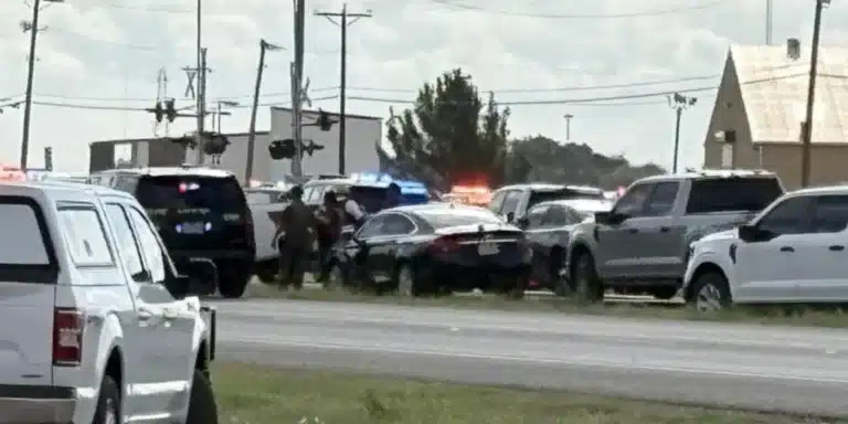 Emergency scene on a highway with police cars and flashing lights amid several parked vehicles, three or more officers assisting near the center.