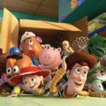 Group of Toy Story characters (Woody, Buzz, Jessie, Hamm, Rex, and friends) crowding around a cardboard box in a colorful playroom, looking curious and ready for adventure.