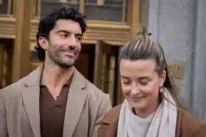 A man and a woman walk side by side outside a building, smiling at each other.