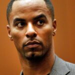 Man in a grey pinstripe suit, looking to his left with a focused expression.