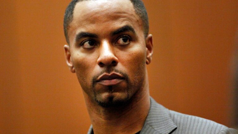Man in a grey pinstripe suit, looking to his left with a focused expression.