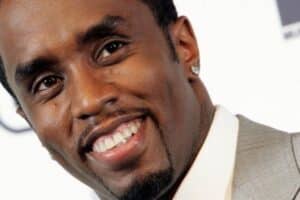 Close-up of a man in a light gray suit smiling at the camera, with a small earring visible.