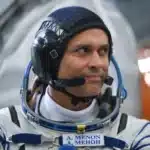 Astronaut in a white spacesuit wearing a black headset, looking to the right.