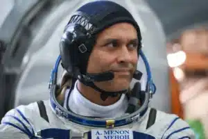 Astronaut in a white spacesuit wearing a black headset, looking to the right.