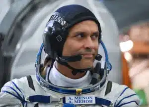 Astronaut in a white spacesuit wearing a black headset, looking to the right.