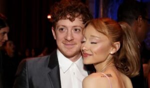 Man in a tuxedo and a woman in a pink dress pose closely at a formal event, smiling gently at the camera.