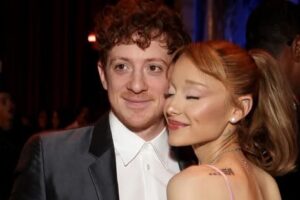 Man in a tuxedo and a woman in a pink dress pose closely at a formal event, smiling gently at the camera.