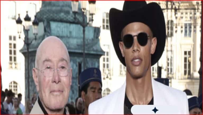 Two men walk outdoors at a busy urban event: one bald with glasses, the other wearing a black wide-brim hat and round sunglasses in a white jacket.