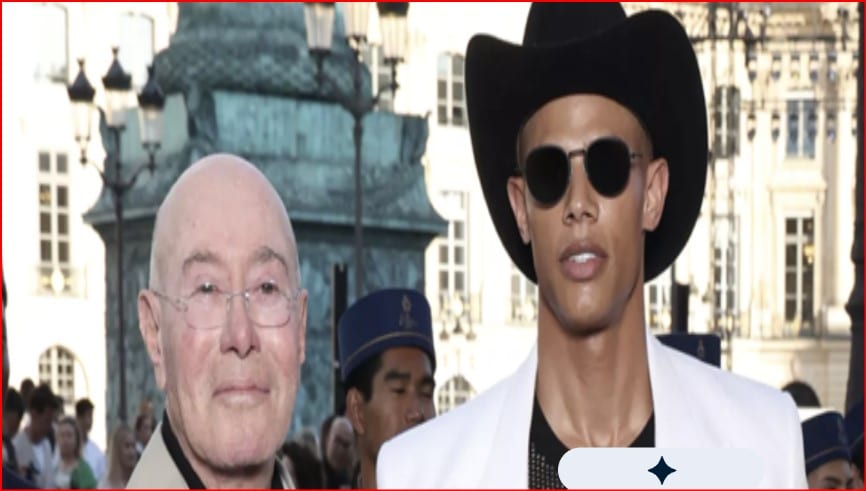 Two men walk outdoors at a busy urban event: one bald with glasses, the other wearing a black wide-brim hat and round sunglasses in a white jacket.