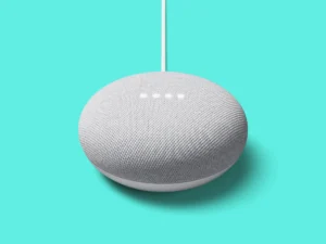 Close-up of a gray fabric-coated spherical smart speaker hanging from a white cable against a bright turquoise background.